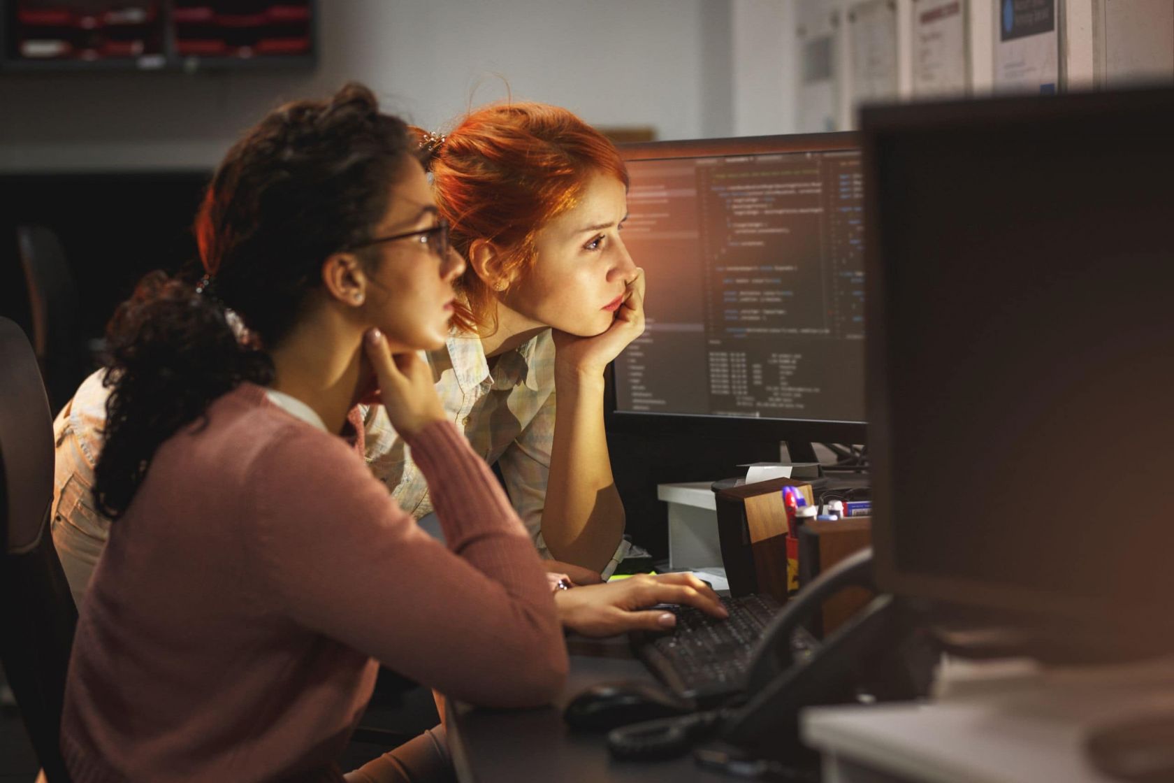 Zwei Frauen sitzen an einem Schreibtisch und arbeiten gemeinsam an einem PC.