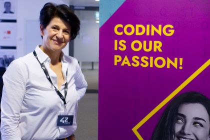 Rosemarie Pichler steht lächelnd neben einem Banner von "42 Vienna" mit der Aufschrift "Coding is our Passion!".