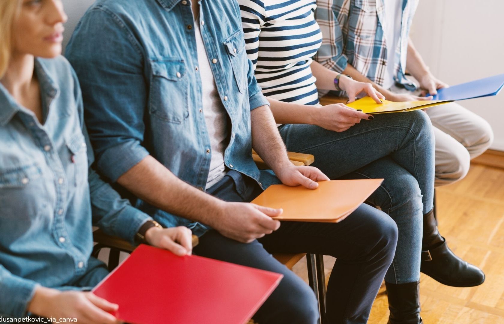 Vier junge Menschen sitzen nebeneinander und warten auf ein Bewerbungsgespräch.