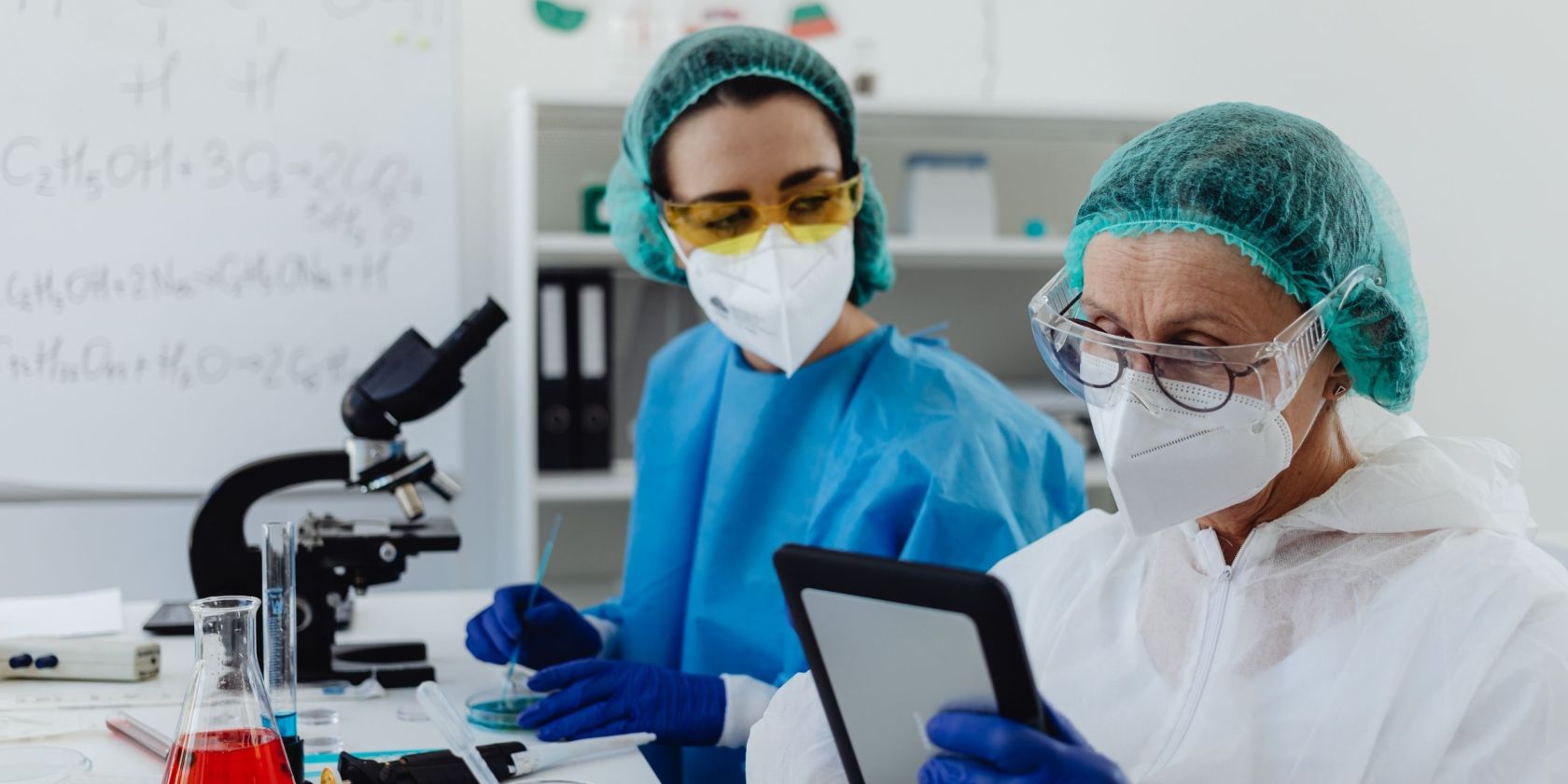 Zwei Frauen in Laborkleidung arbeiten an einem Labortisch.