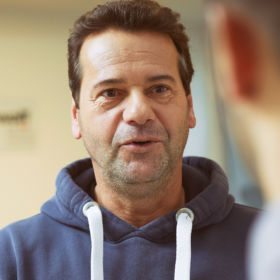 Ein Mann mit Kapuzenpullover freut sich, mit Hilfe der Arbeitsstiftung des waff einen neuen Job gefunden zu haben.