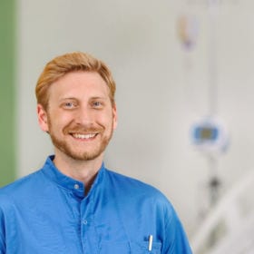 Bild zeigt einen Krankenpfleger vor einem leeren Spitalsbett