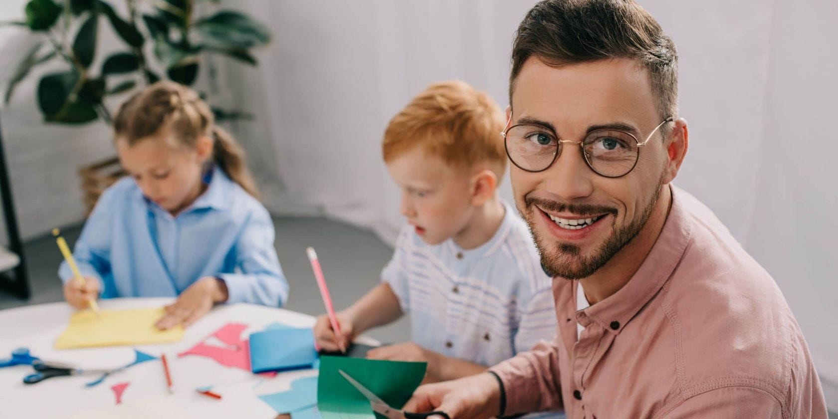 Elementarpädagoge bastelt mit zwei kleinen Kindern mit buntem Papier.