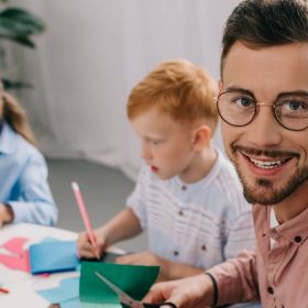 Elementarpädagoge bastelt mit zwei kleinen Kindern mit buntem Papier.