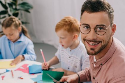 Elementarpädagoge bastelt mit zwei kleinen Kindern mit buntem Papier.