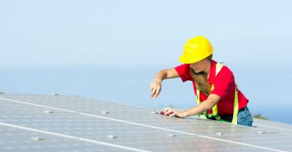 Frau mit gelbem Schutzhelm schraubt auf einem Solardach Klimarelevante Berufe - Green Jobs