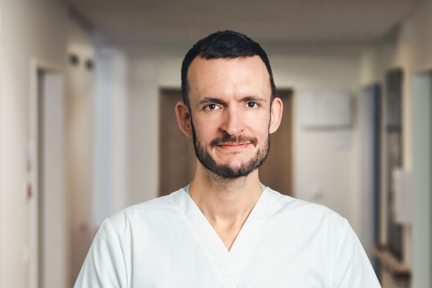 Ein Pfleger in einem weißen Arbeitsmantel scahut in die Kamera.