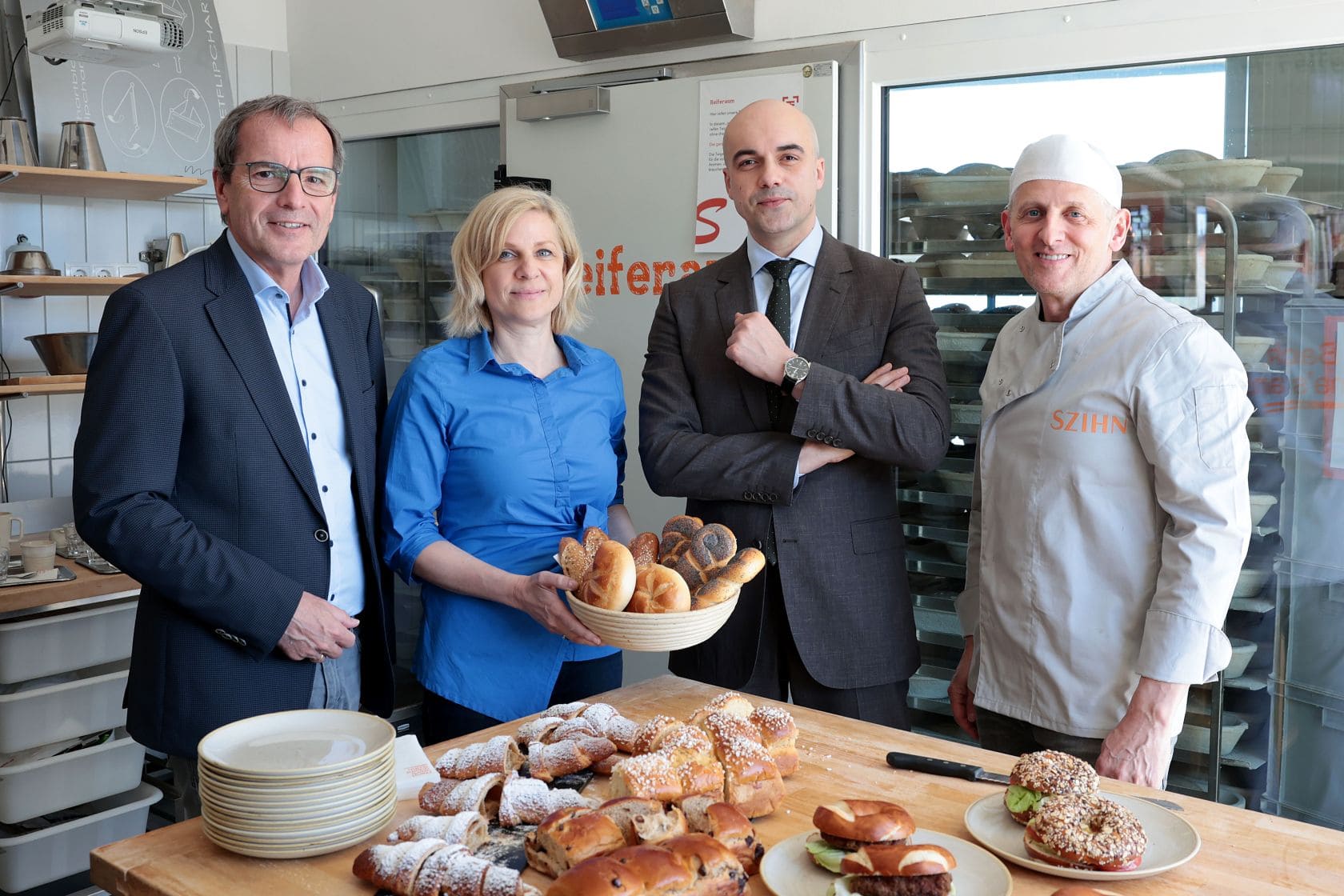 Christian Meidlinger, Alexandra und Stefan Szihn und Marko Miloradovic stehen hinter einem Tisch mit Backwaren in einer Bäckereie